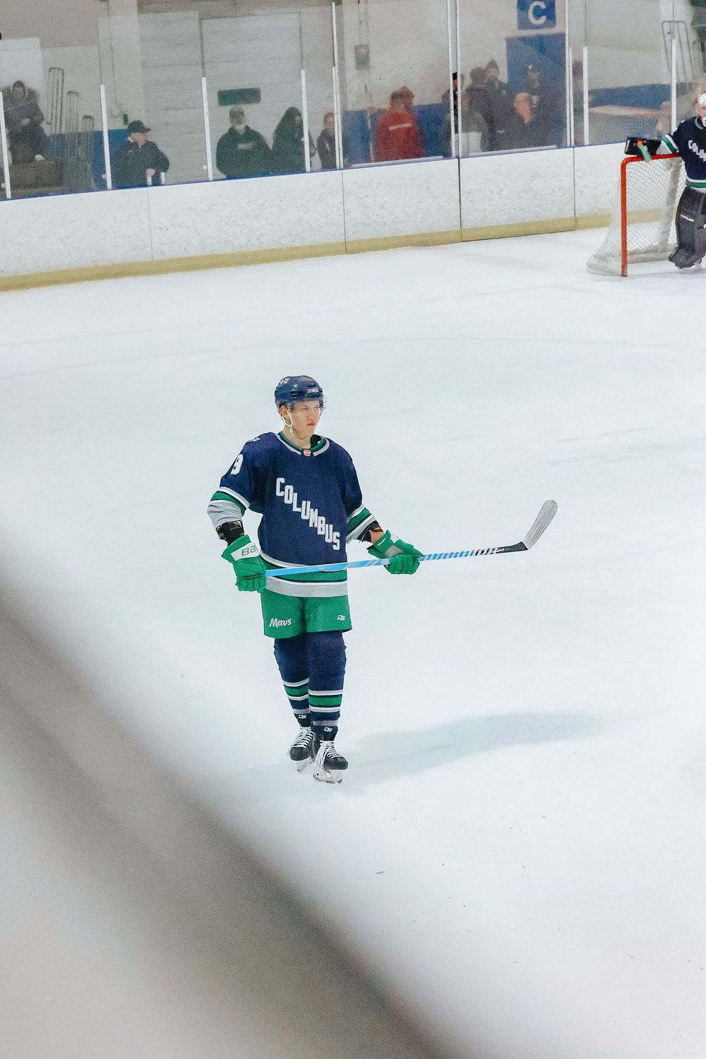 Hockey player in blue and green jersey skating on ice rink during practice session.