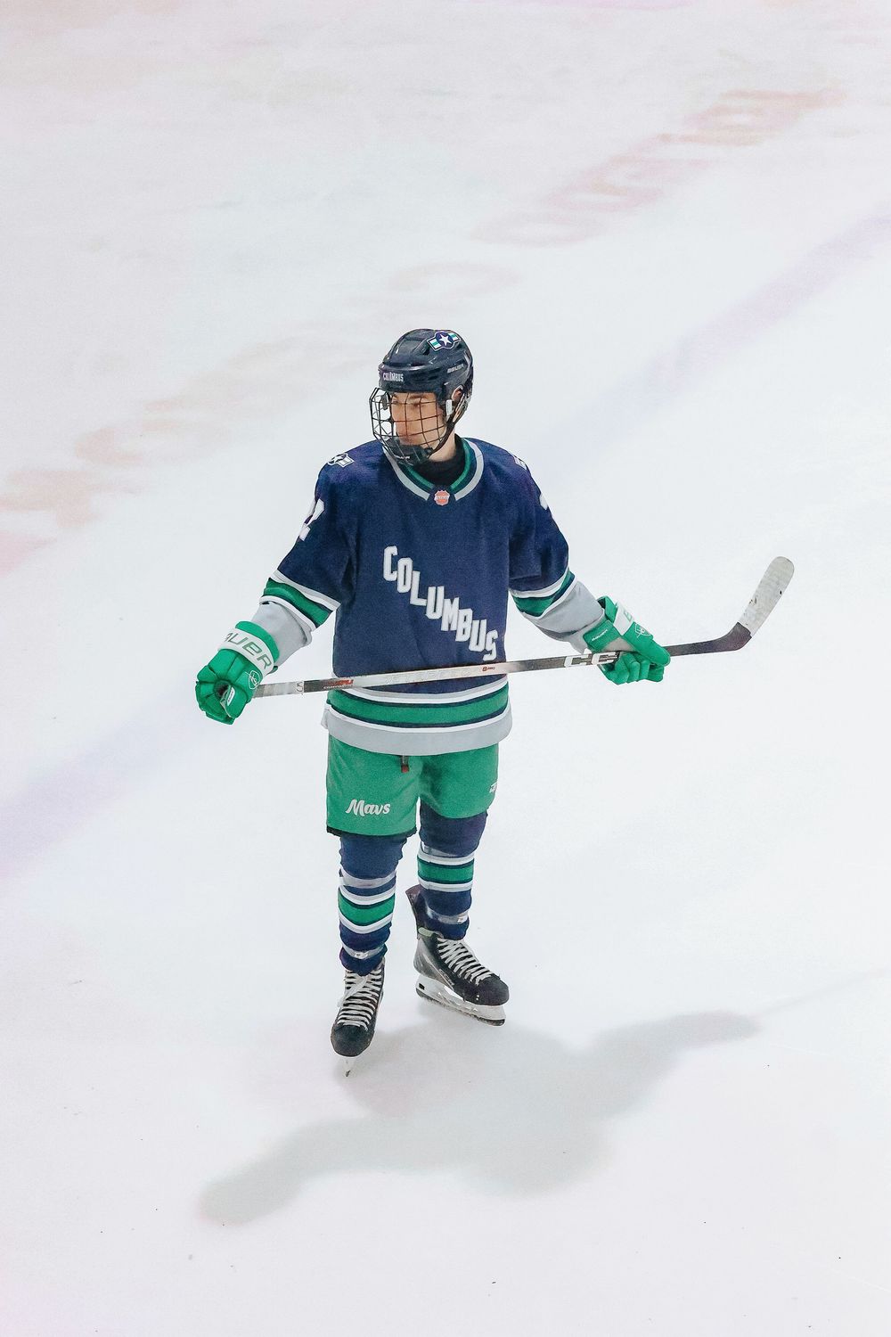 Hockey player in navy and green uniform skating on ice during game action.