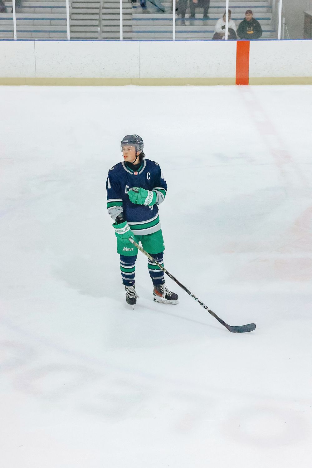 Hockey player in blue and green uniform skating with stick on ice rink during game.