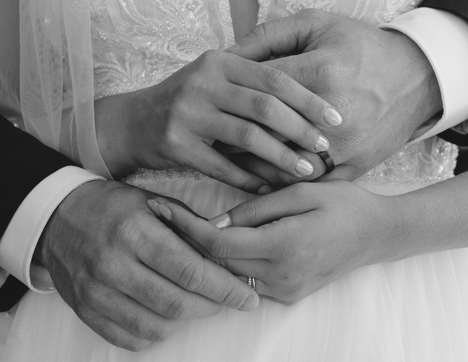 A bride and groom exchanging their rings lovingly over the brides dress.