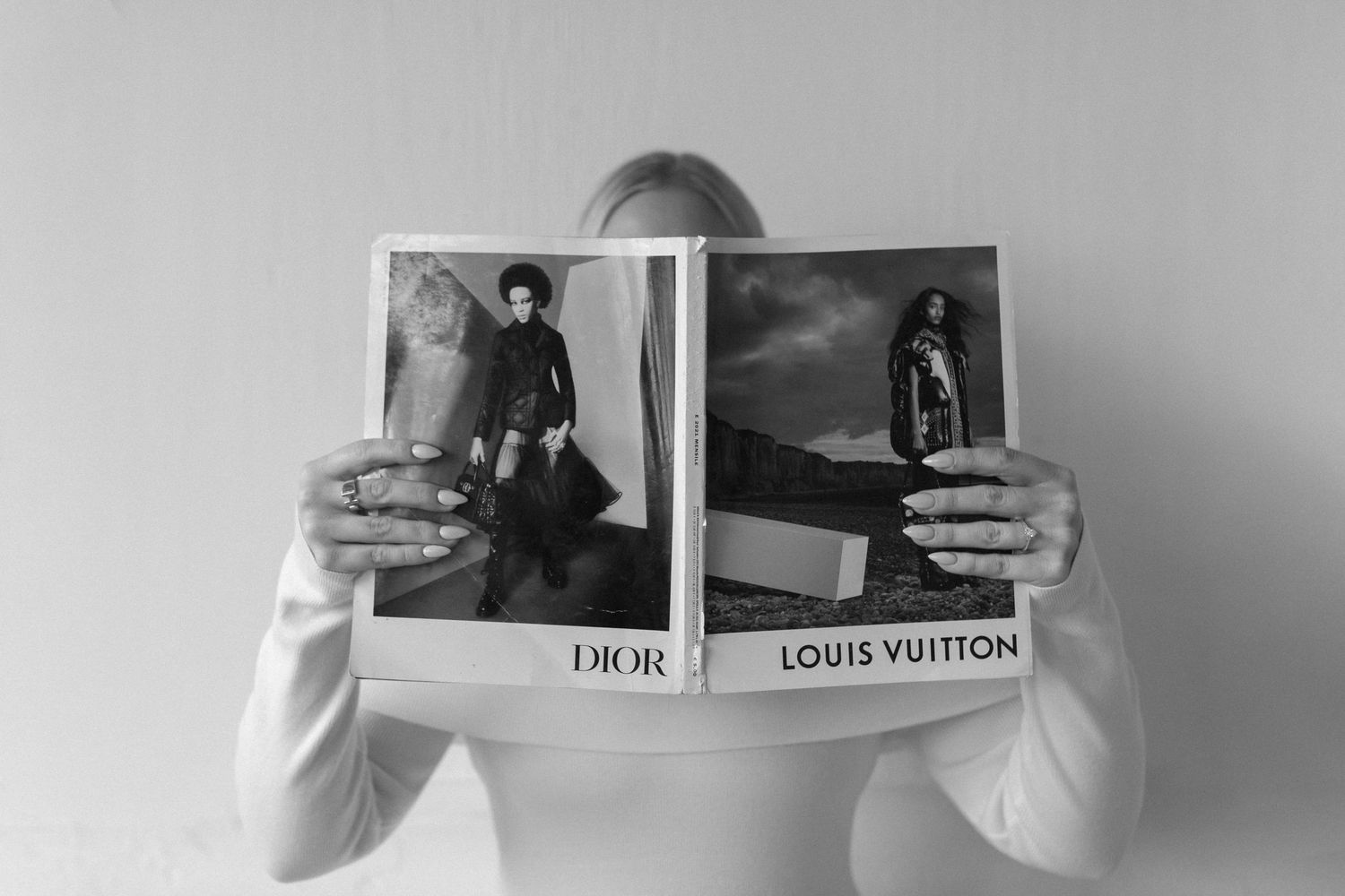 Person holding open Dior and Louis Vuitton fashion magazine in black and white photo.