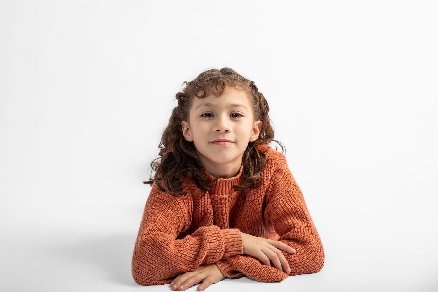 A portrait of a youthful subject in a rust-colored sweater against a white background.