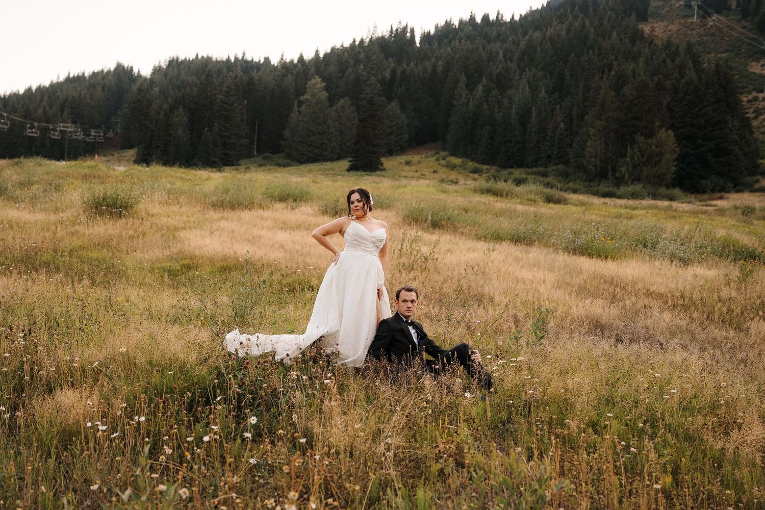 Person in a white dress twirls through a golden mountain meadow with evergreen forest in the background.