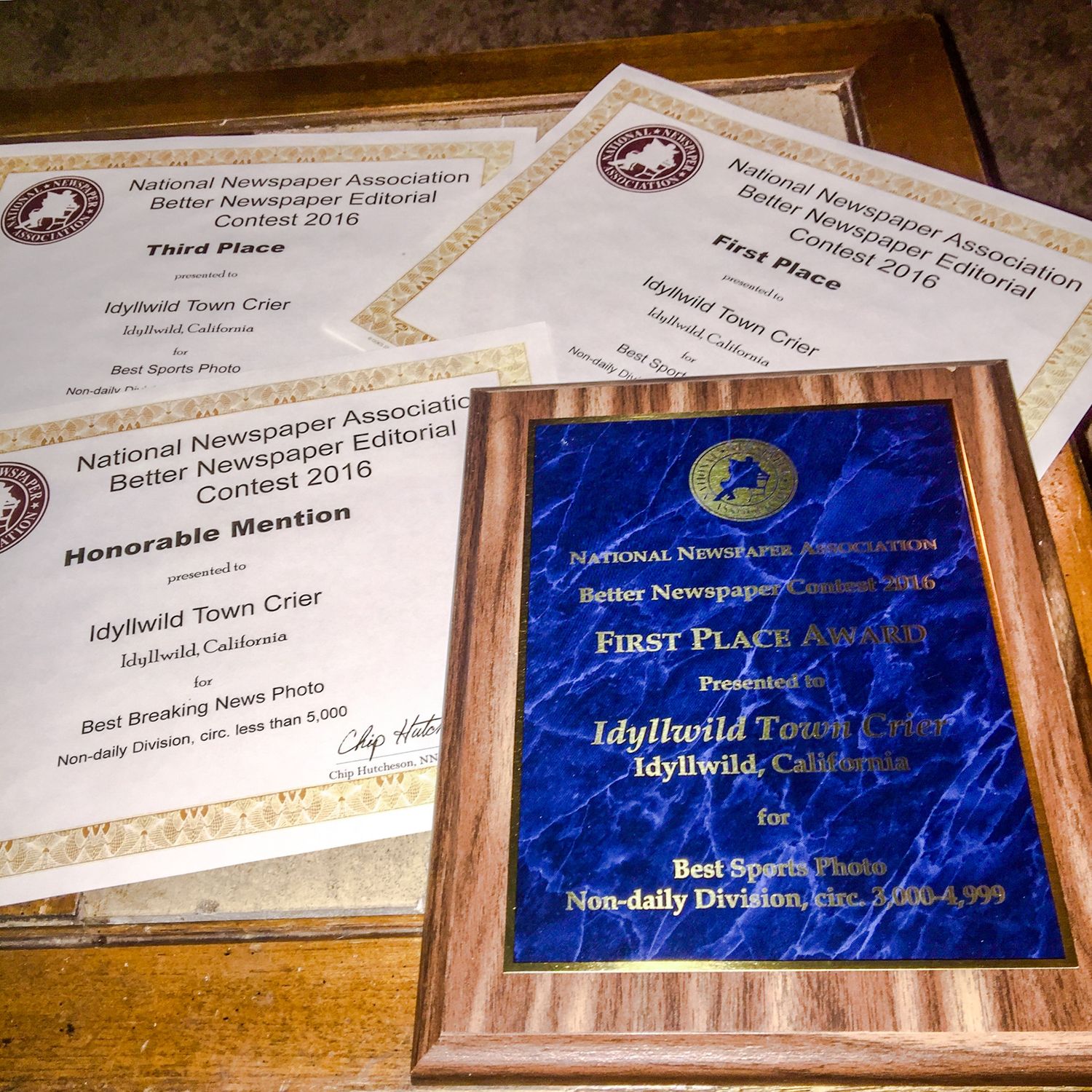 Multiple award plaques and certificates with blue and gold accents displayed on a wooden surface.