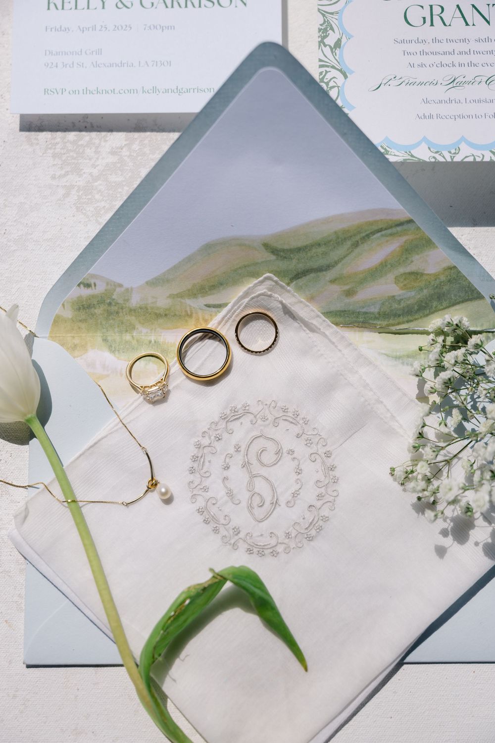 Wedding flat lay with gold rings, monogrammed handkerchief, invitations, and white tulip.