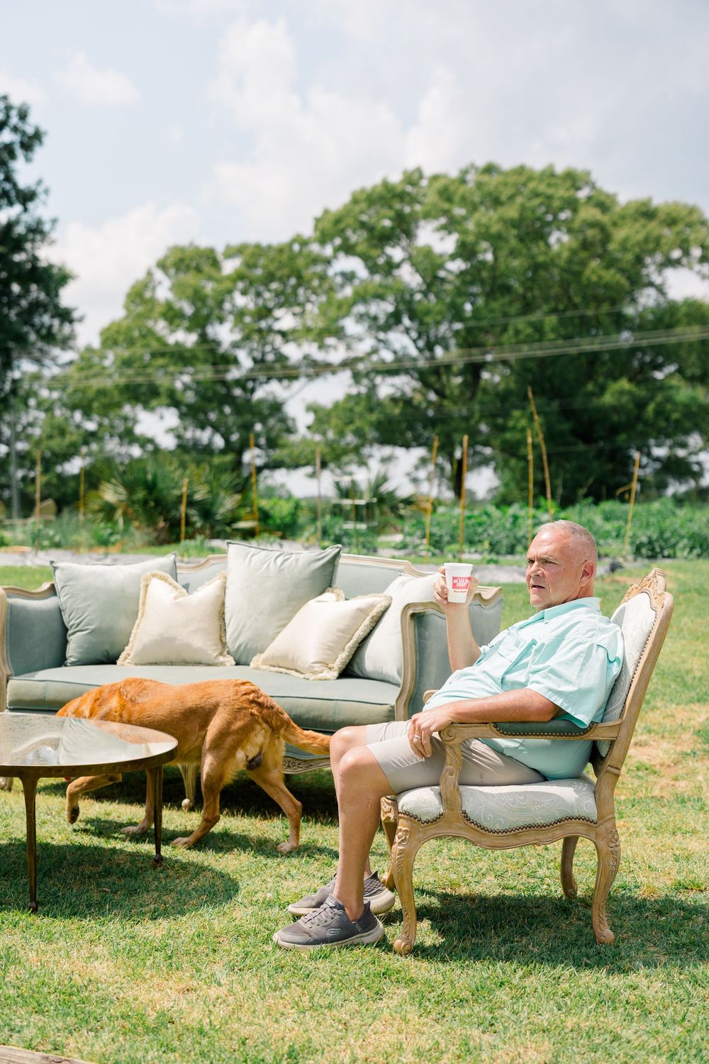 Senior man relaxing outdoors on lawn furniture with a golden dog nearby.