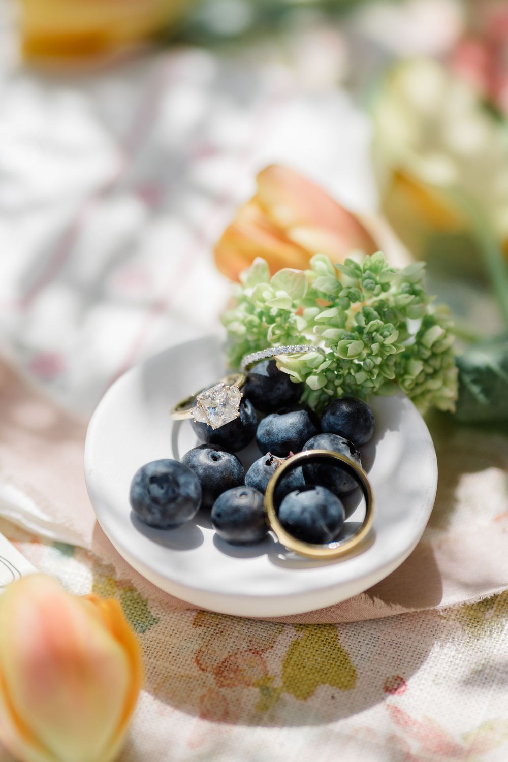 Wedding rings and diamond engagement ring displayed on white dish with fresh blueberries.