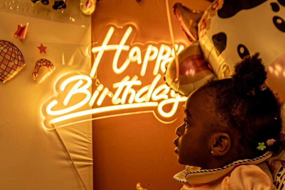 Glowing neon birthday sign illuminates a wall with warm orange lighting in a festive party setting.
