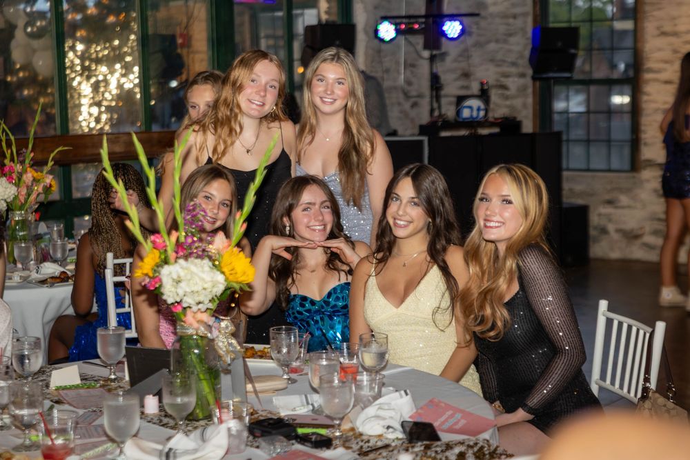 A group poses together at an elegant dinner table with floral centerpieces and wine glasses in a rustic venue.