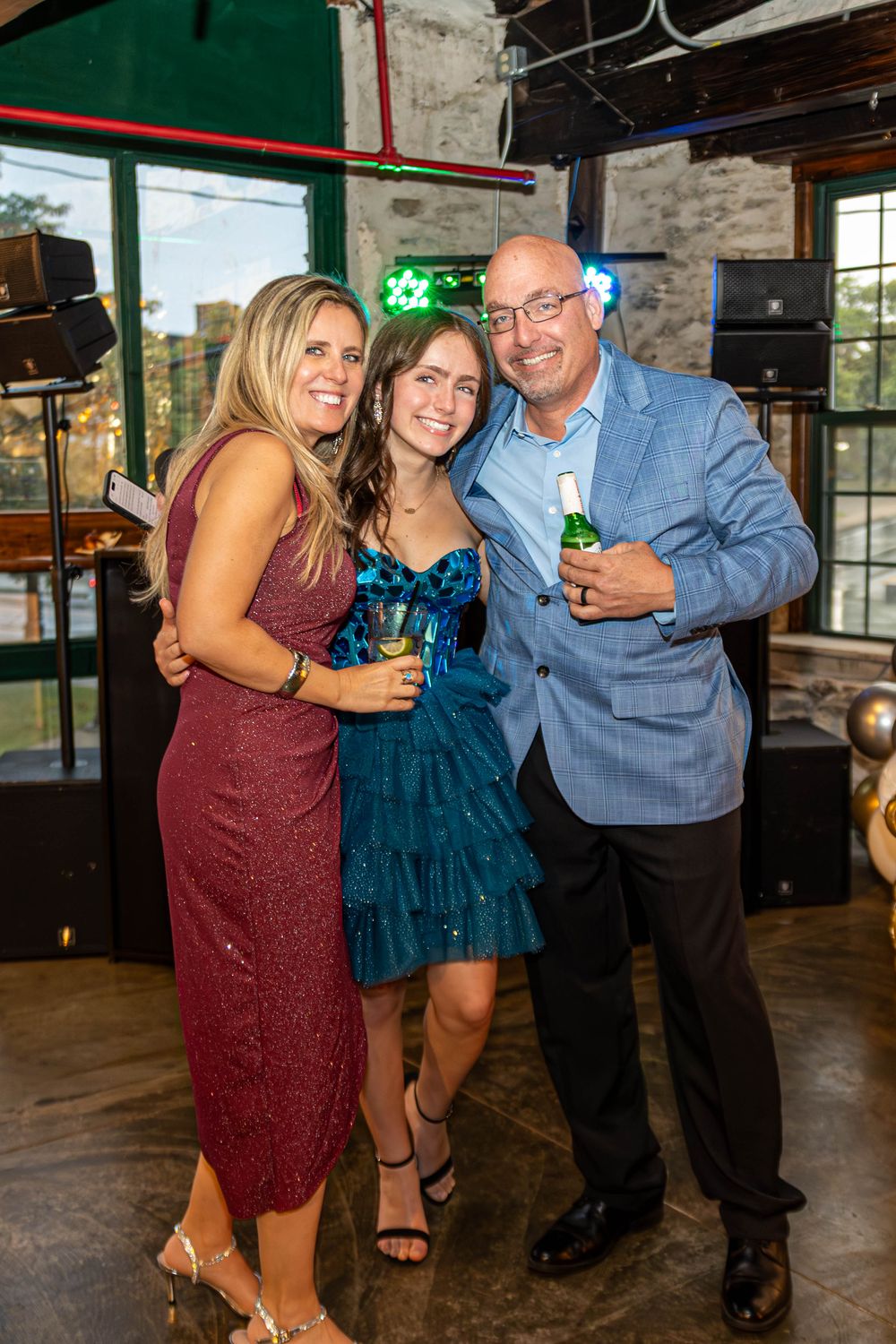 Three people dancing and smiling together at a party in a rustic venue with brick walls and wooden floors.