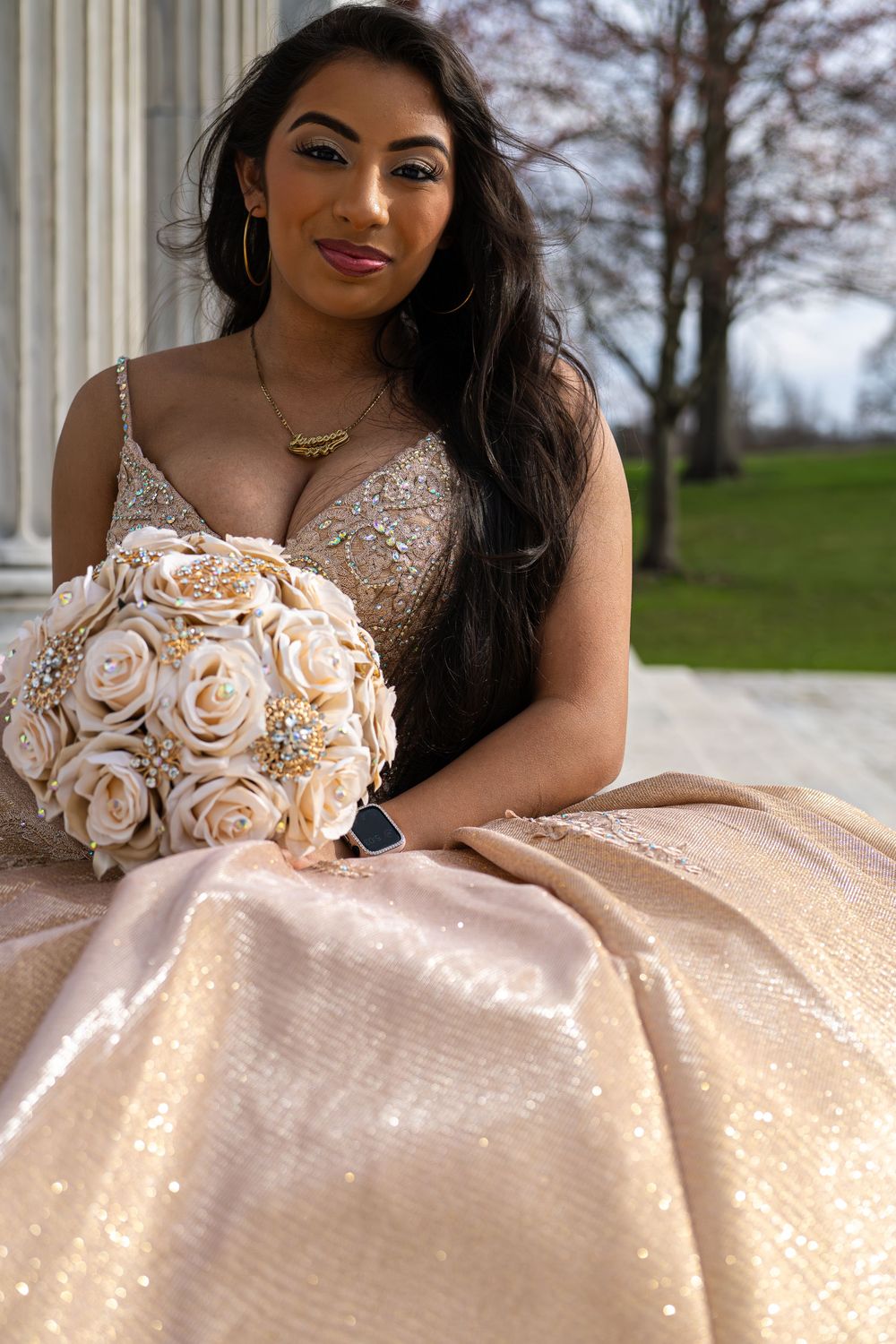 A person in a blush pink sequined ballgown poses outdoors with delicate rose details on the bodice.