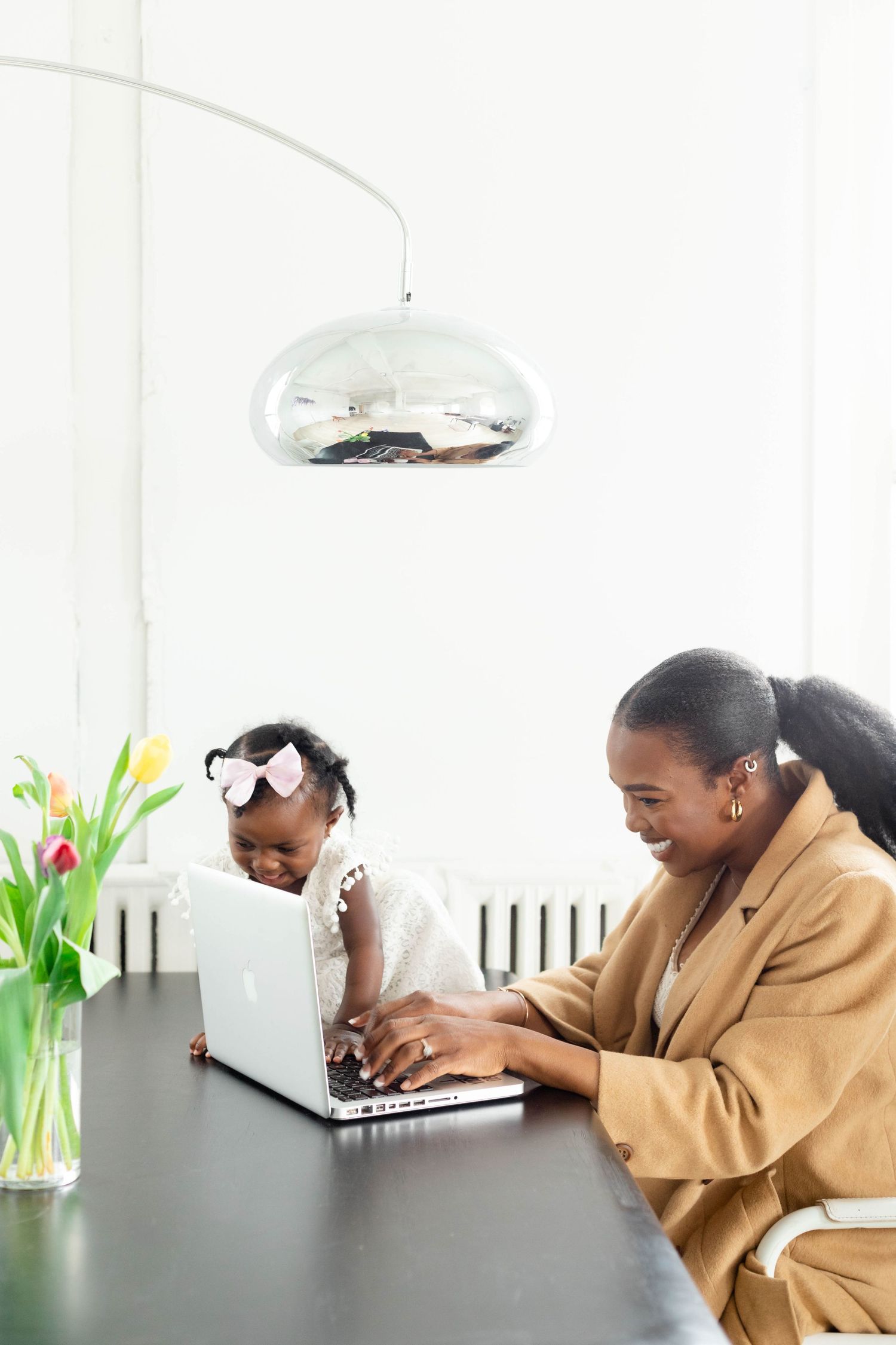 Person in tan hoodie showing different emotional expressions while using laptop at desk with flowers in background.