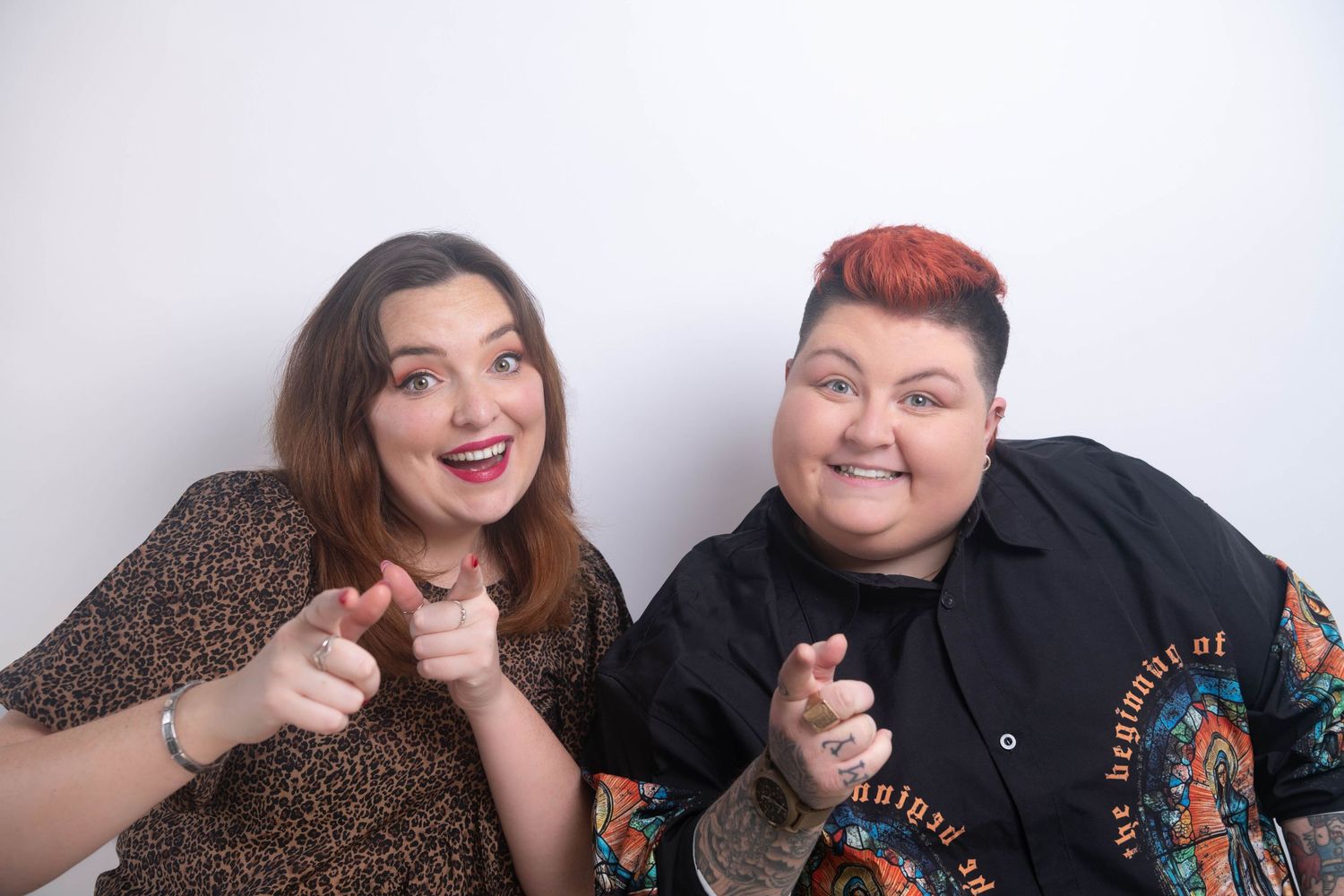 Two women smiling and pointing at camera, one in leopard print top and one in black jacket.