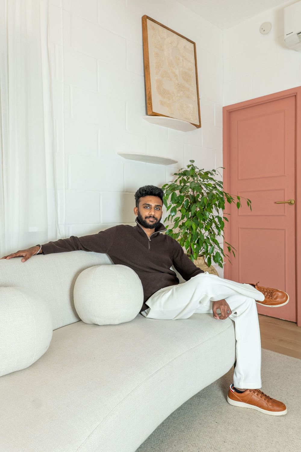 Three sequential photos show someone lounging casually on a white couch in a minimalist room with pink doors and plants.