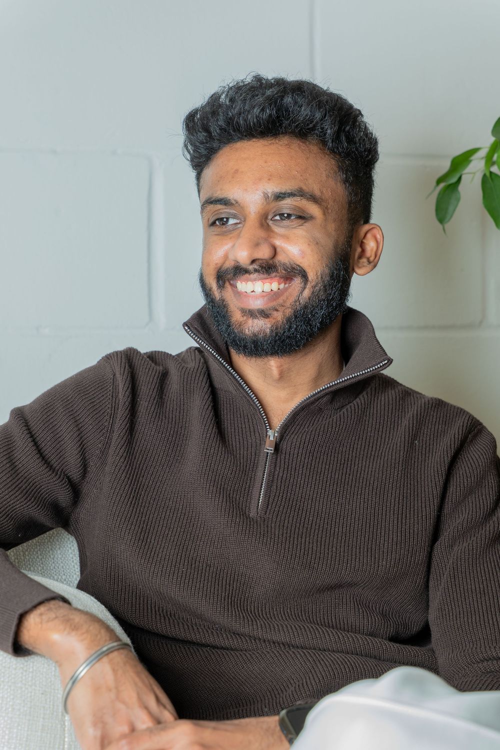 Person in brown sweater shown in multiple poses sitting and smiling against a white wall.