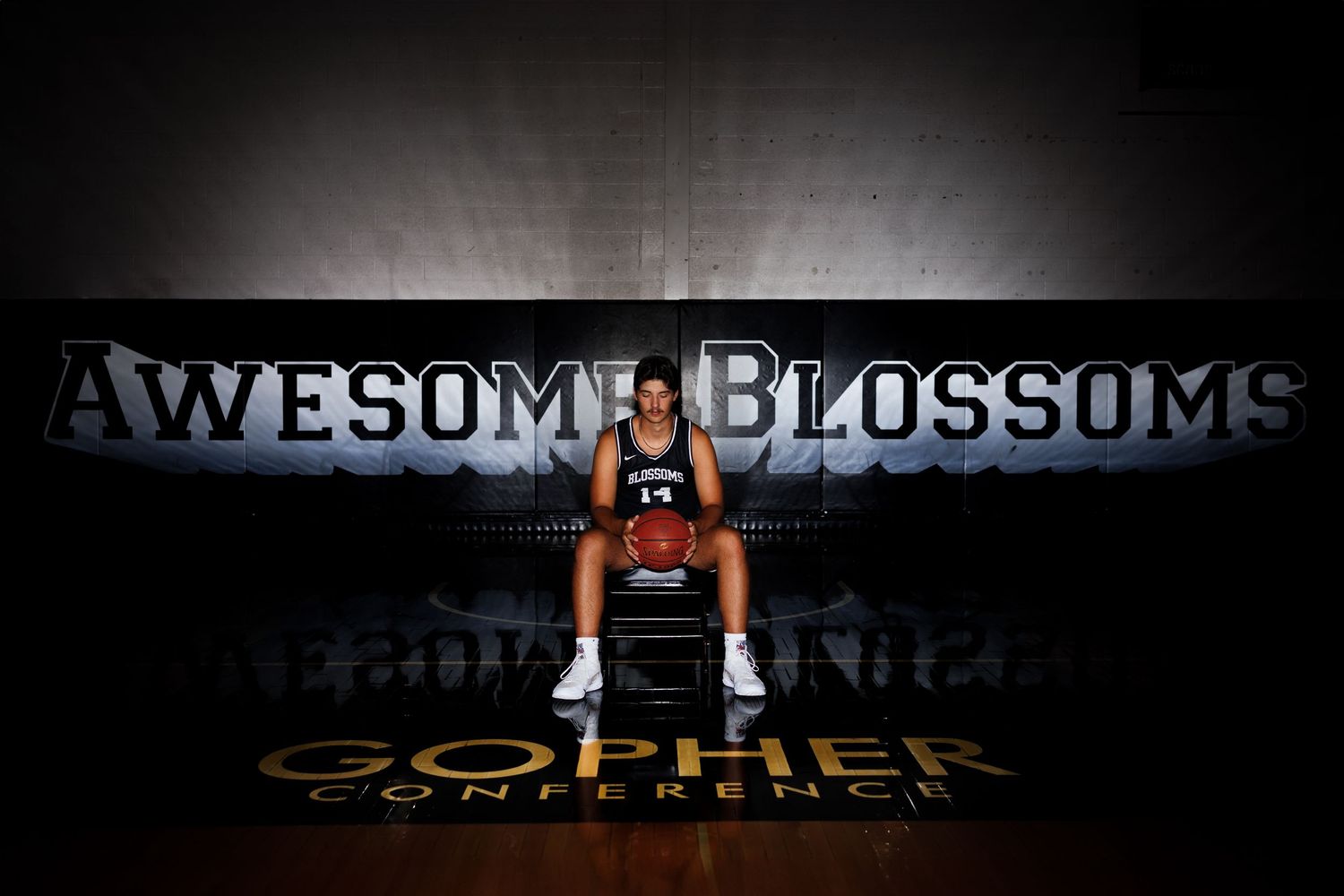 Senior basketball player in split stance performing an intense workout in a dark gym setting with dramatic lighting.