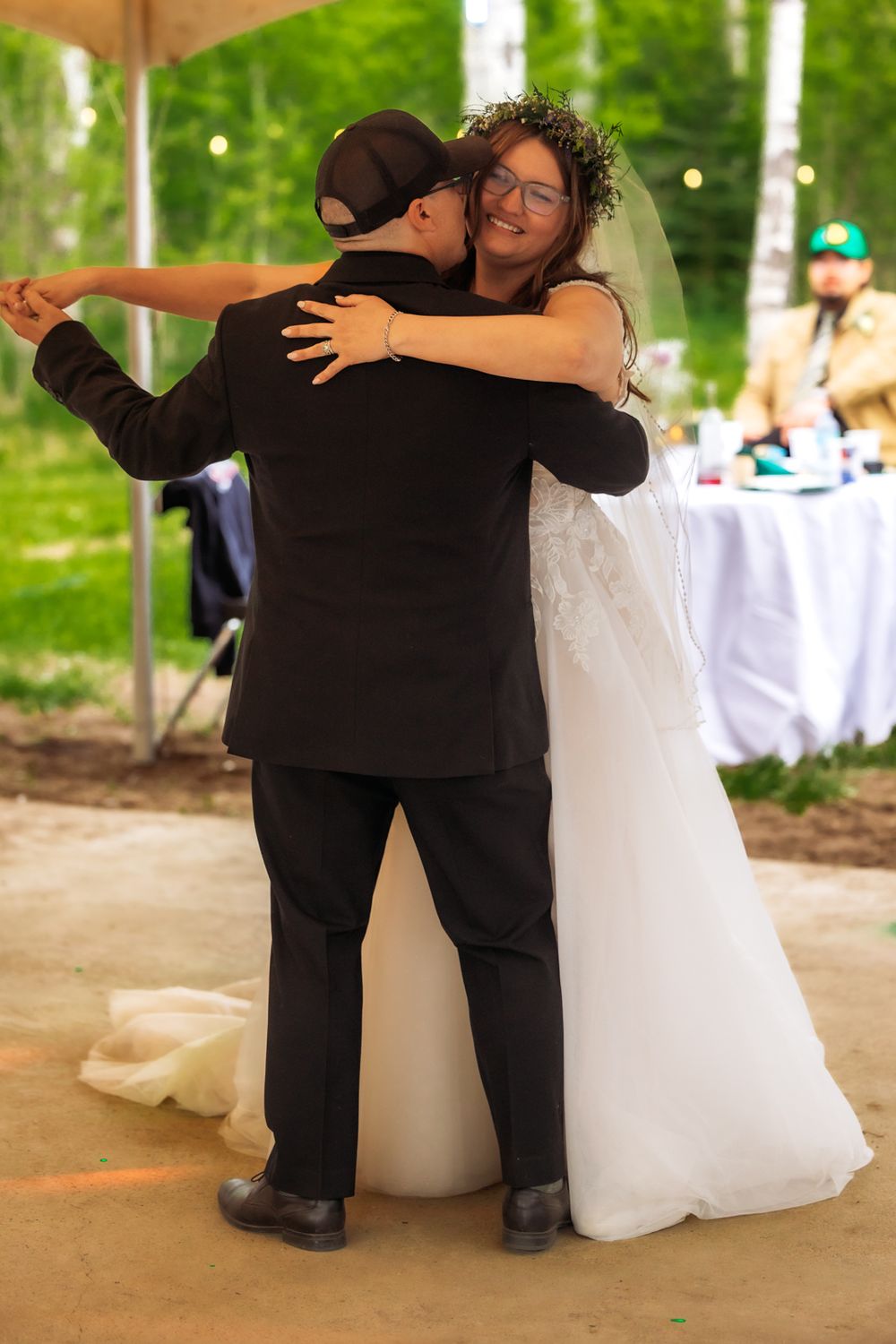 Bride smiling while sharing first dance embrace at outdoor wedding reception.