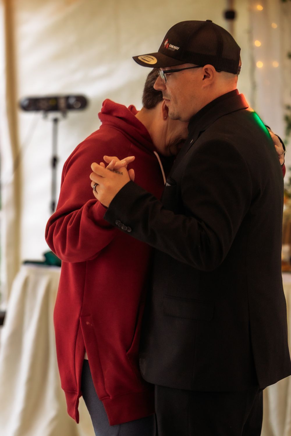 Couple shares a slow dance embrace at wedding reception under a tent with string lights.