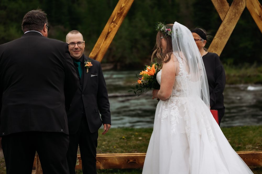 Groom smiling as bride approaches outdoor riverside wedding ceremony altar.