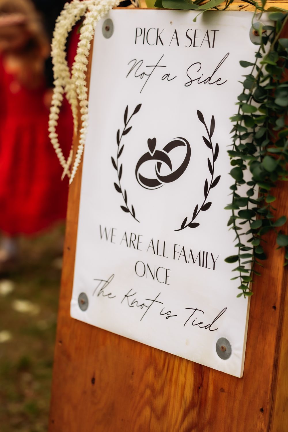 Elegant wedding sign reading Pick a Seat Not a Side, We Are All Family Once the Knot is Tied on wooden stand.