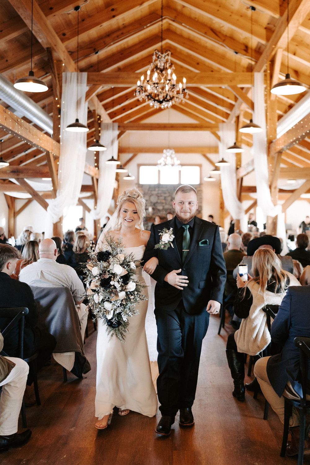 Smiling bride walking down aisle with escort in elegant rustic barn wedding venue.
