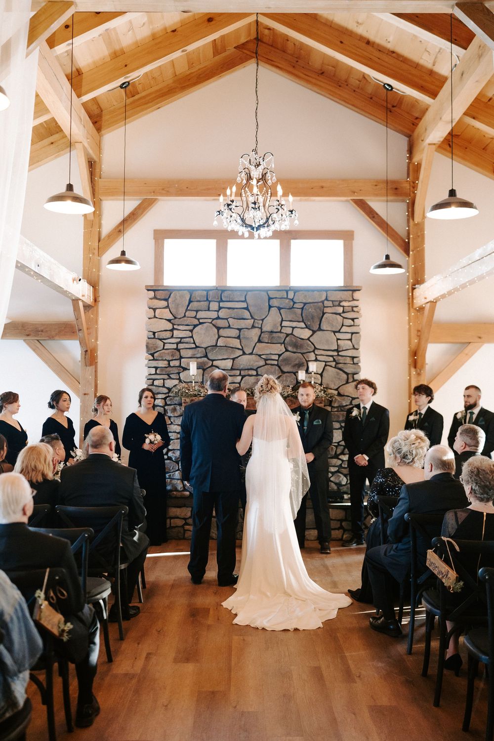 Bride and groom exchange vows at altar before stone fireplace in rustic timber frame wedding venue.