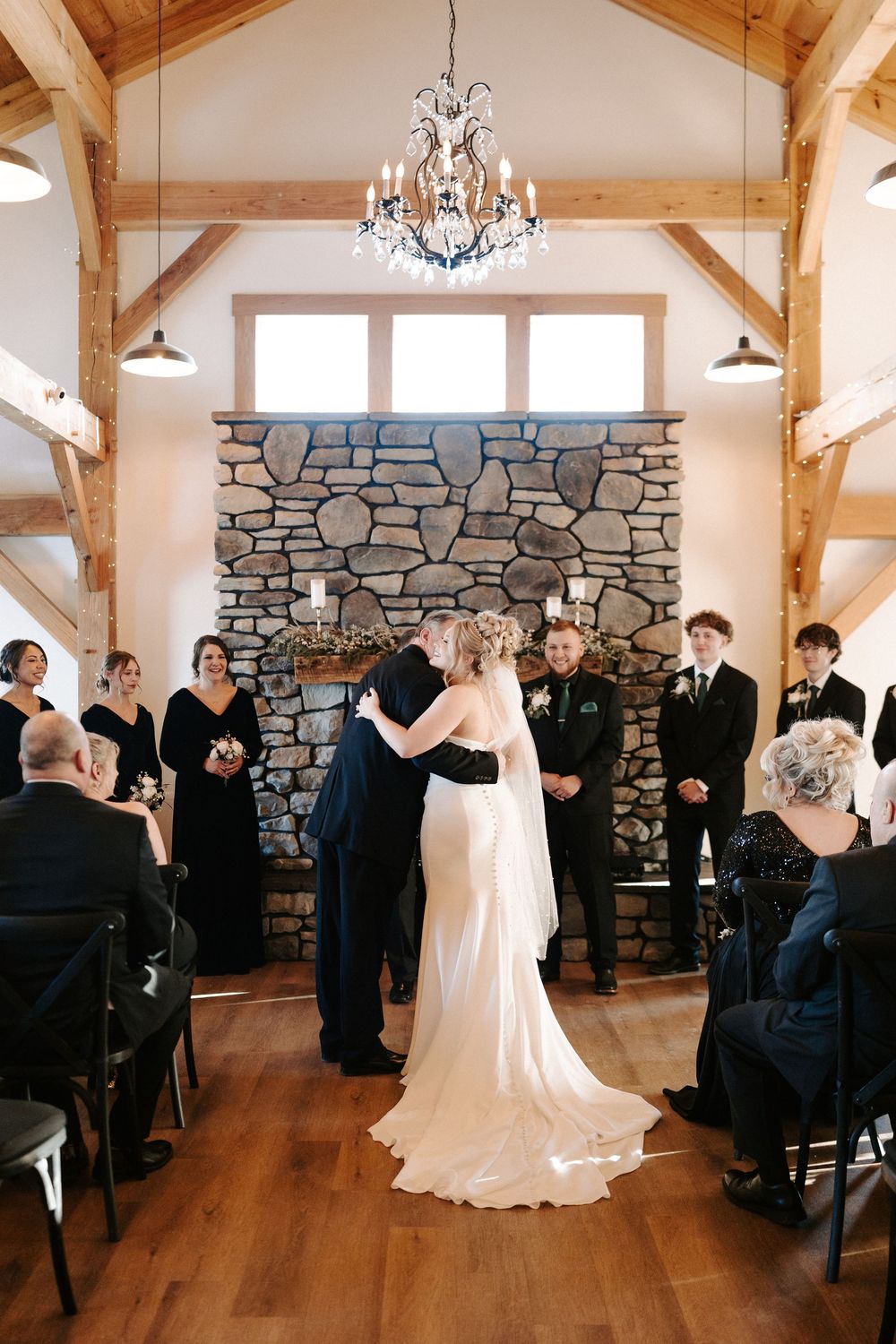 Bride and groom share first kiss at altar before stone fireplace in rustic barn wedding venue.