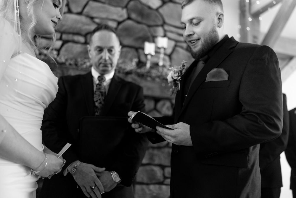 Black and white close-up of groom reading vows during intimate wedding ceremony at stone altar.