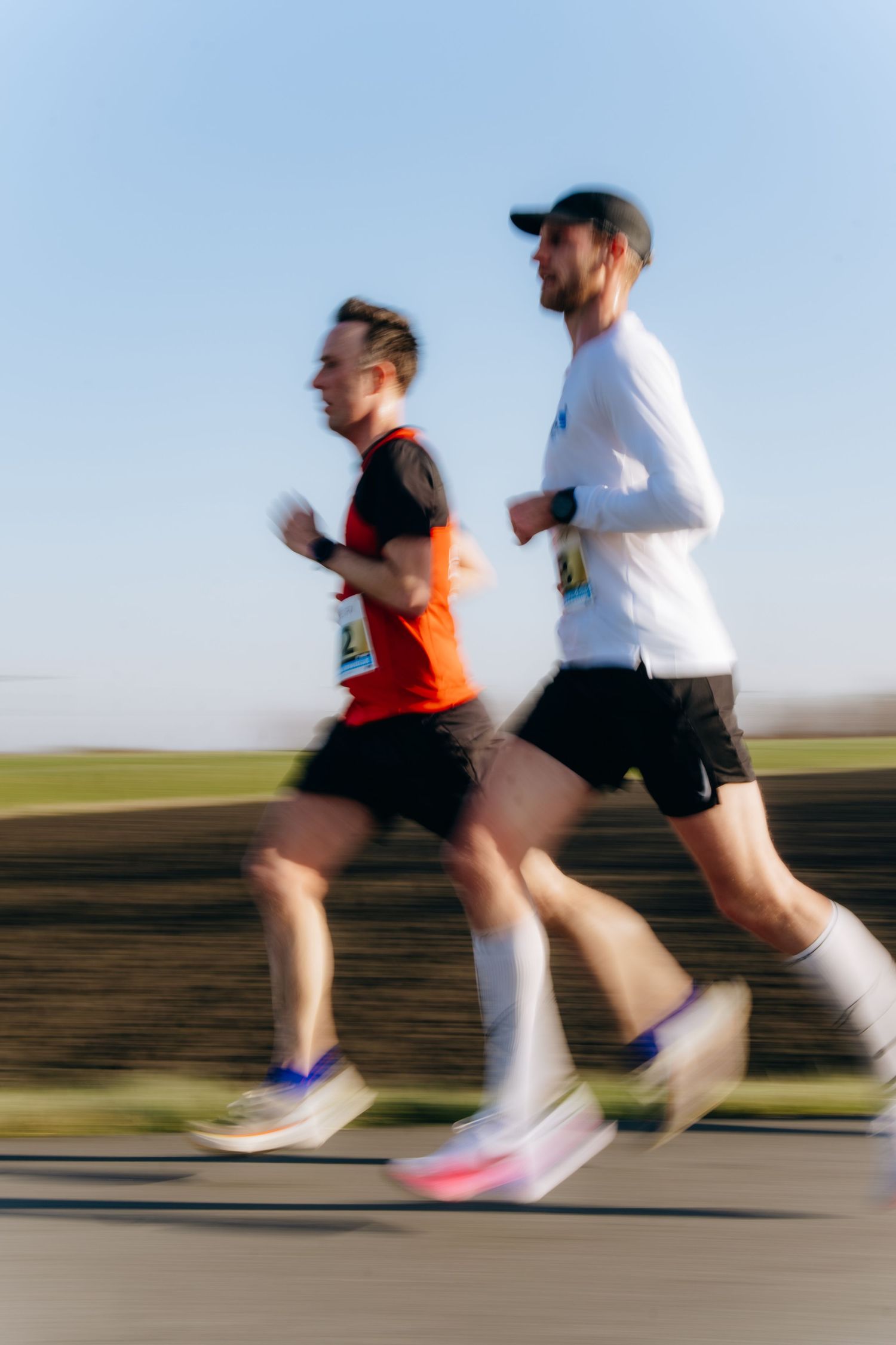 Two male marathon runners racing outdoors with motion blur effect under a clear blue sky.