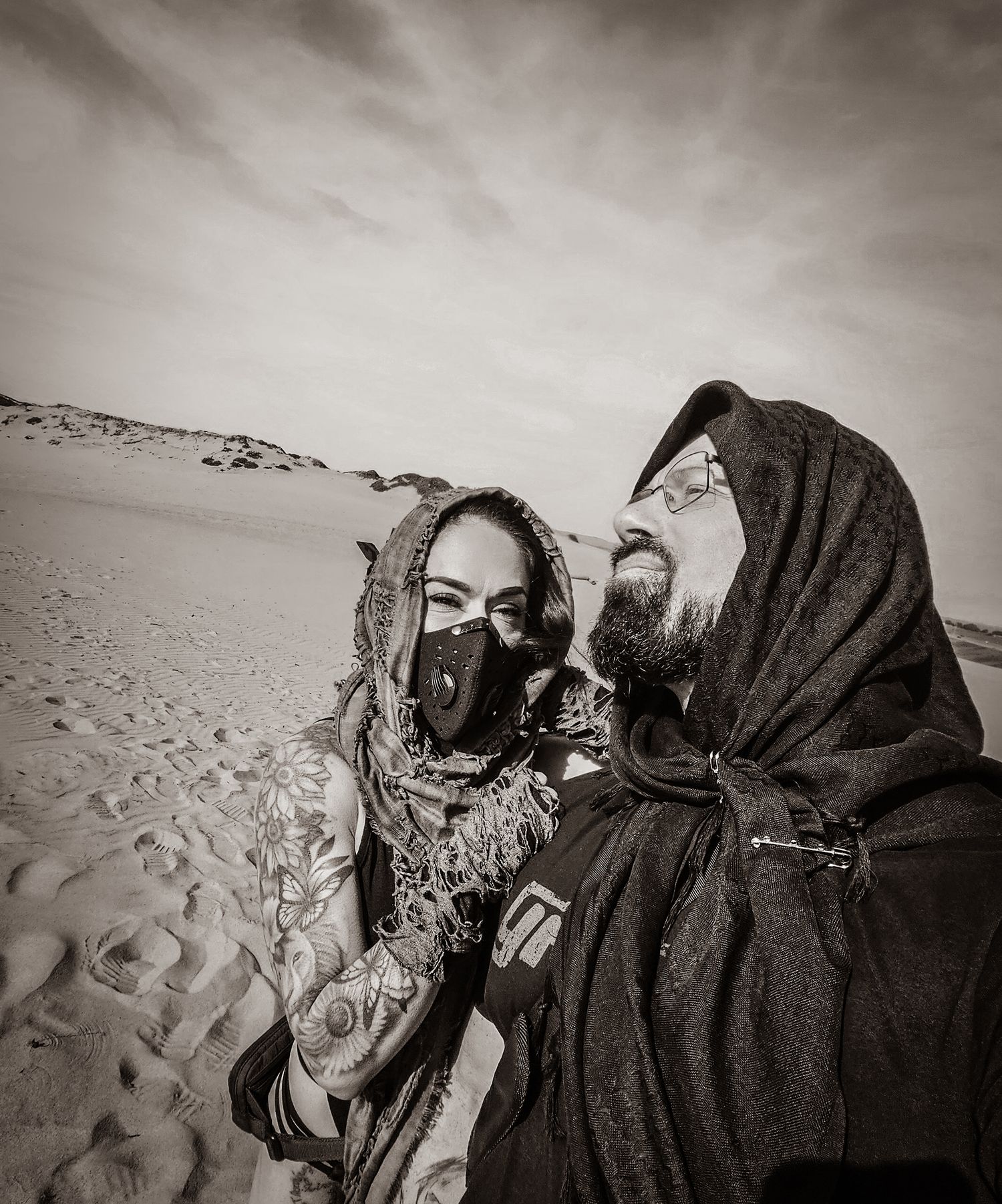 Figures in dark robes traverse a vast desert landscape with dramatic shadows and rippling sand dunes in sepia tones.