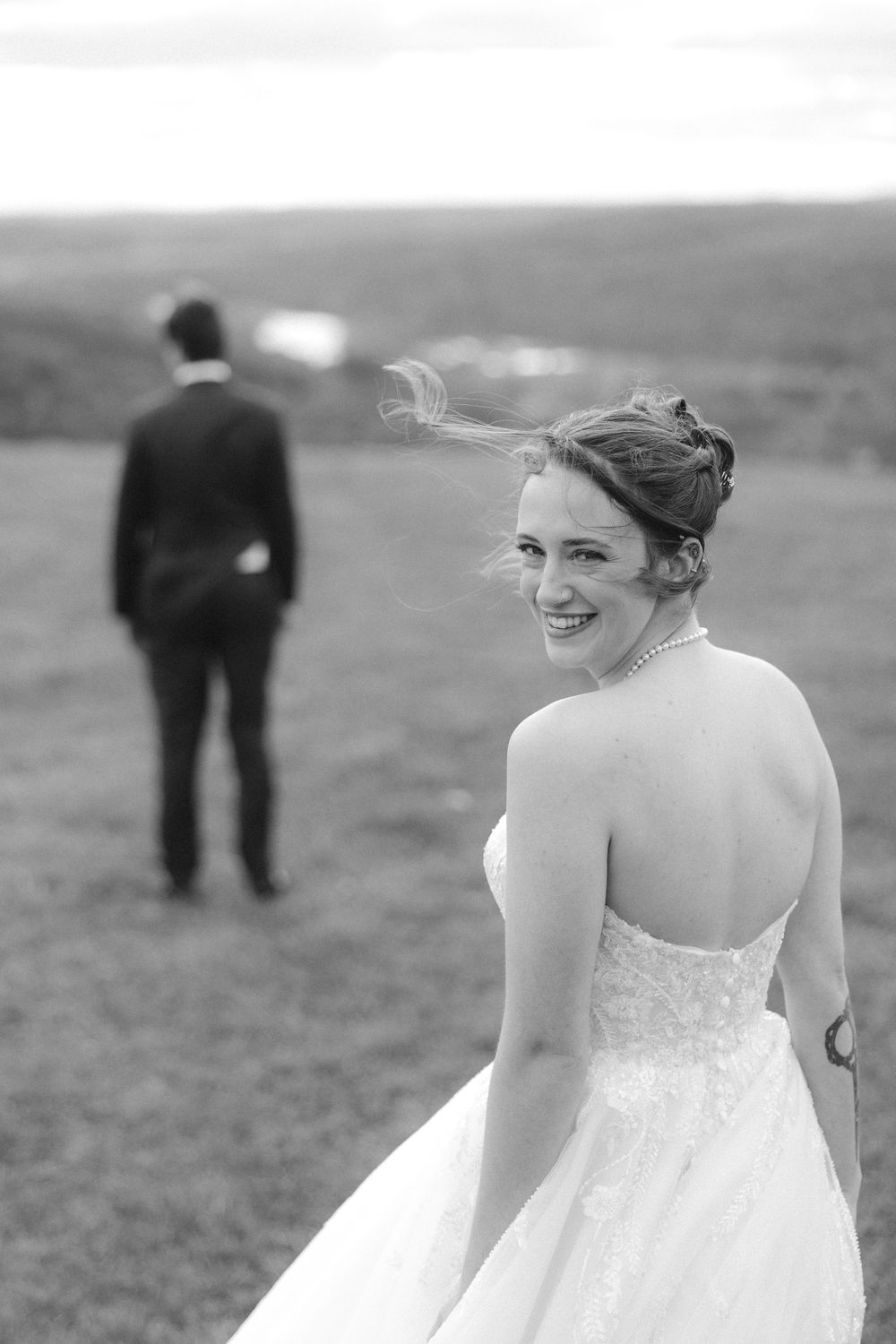 A bride in a white strapless wedding dress smiles joyfully while walking outdoors in black and white photography.