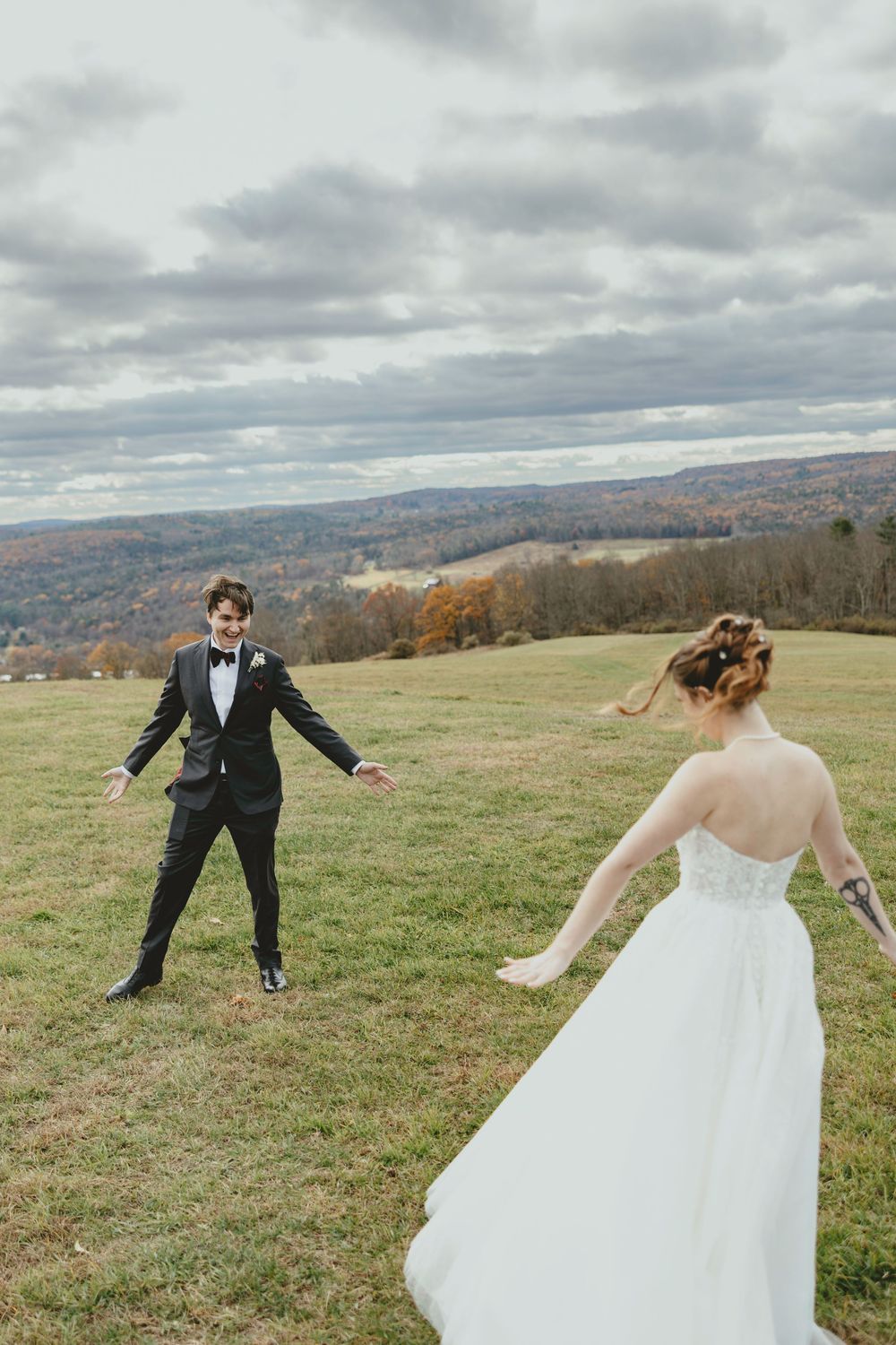 A bride and groom playfully dance apart on a hilltop with a sweeping mountain vista behind them.