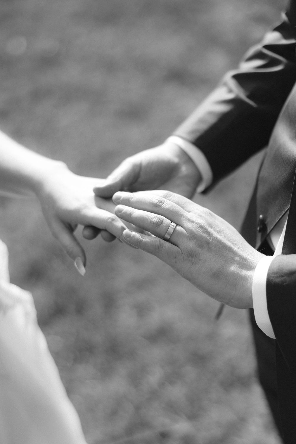 Close-up of newlyweds' hands exchanging wedding rings during an outdoor ceremony in black and white.