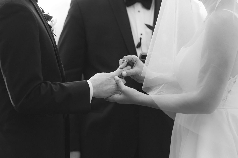 A black and white wedding ceremony photo showing a couple exchanging vows at the altar.
