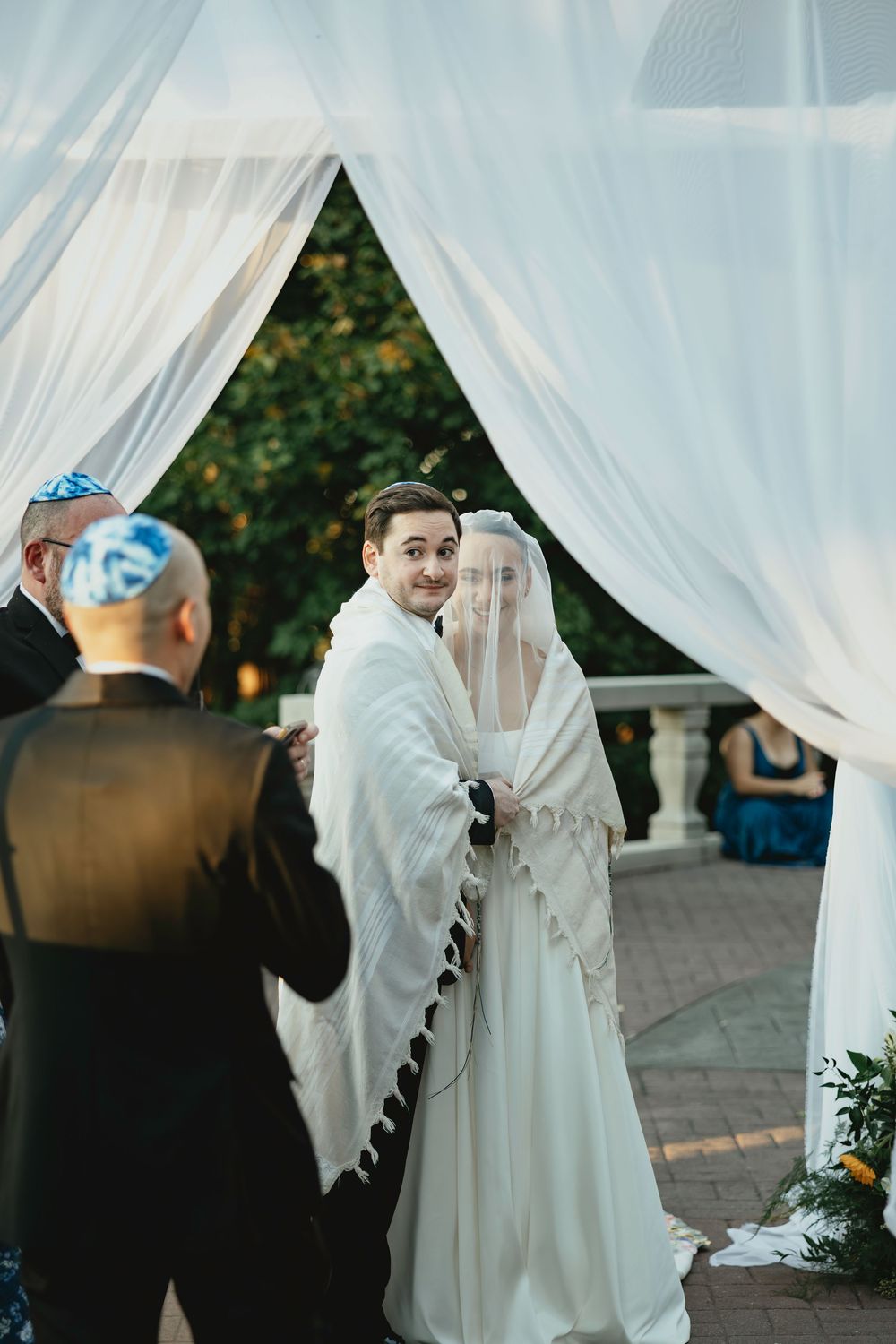 A couple shares an intimate moment under a white fabric canopy during their traditional Jewish wedding ceremony.