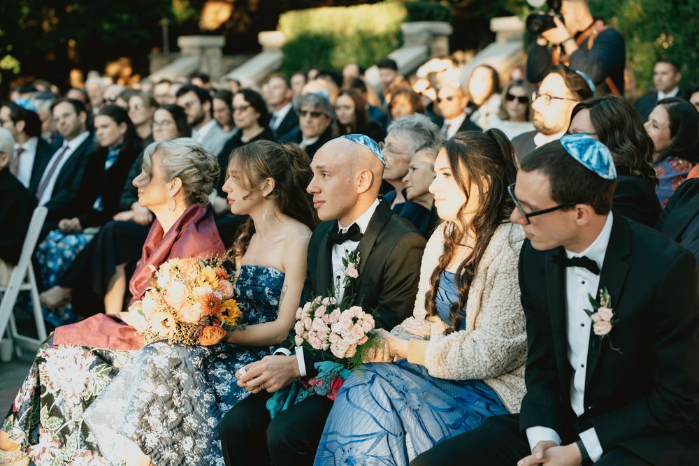 Wedding guests laugh and smile during an outdoor reception celebration at sunset.