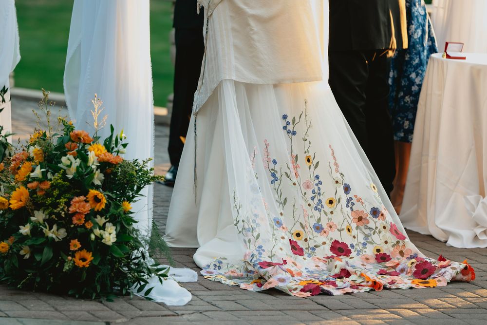 White wedding dress trains and floral arrangements line up in a row during an elegant outdoor ceremony.