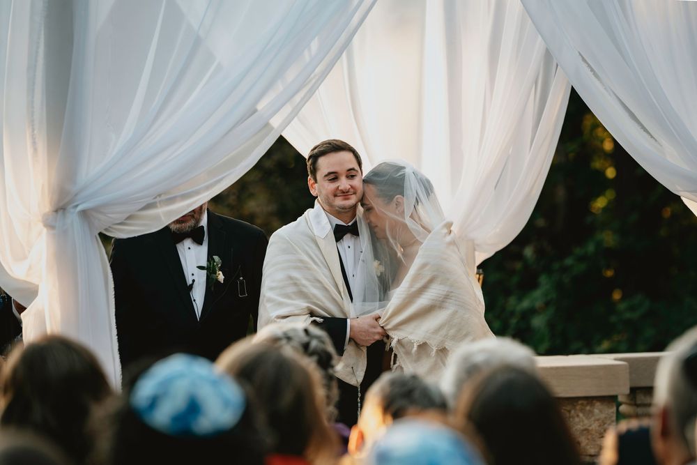 Wedding guests dance and celebrate under an elegant white tent with flowing fabric drapes and twinkling lights.