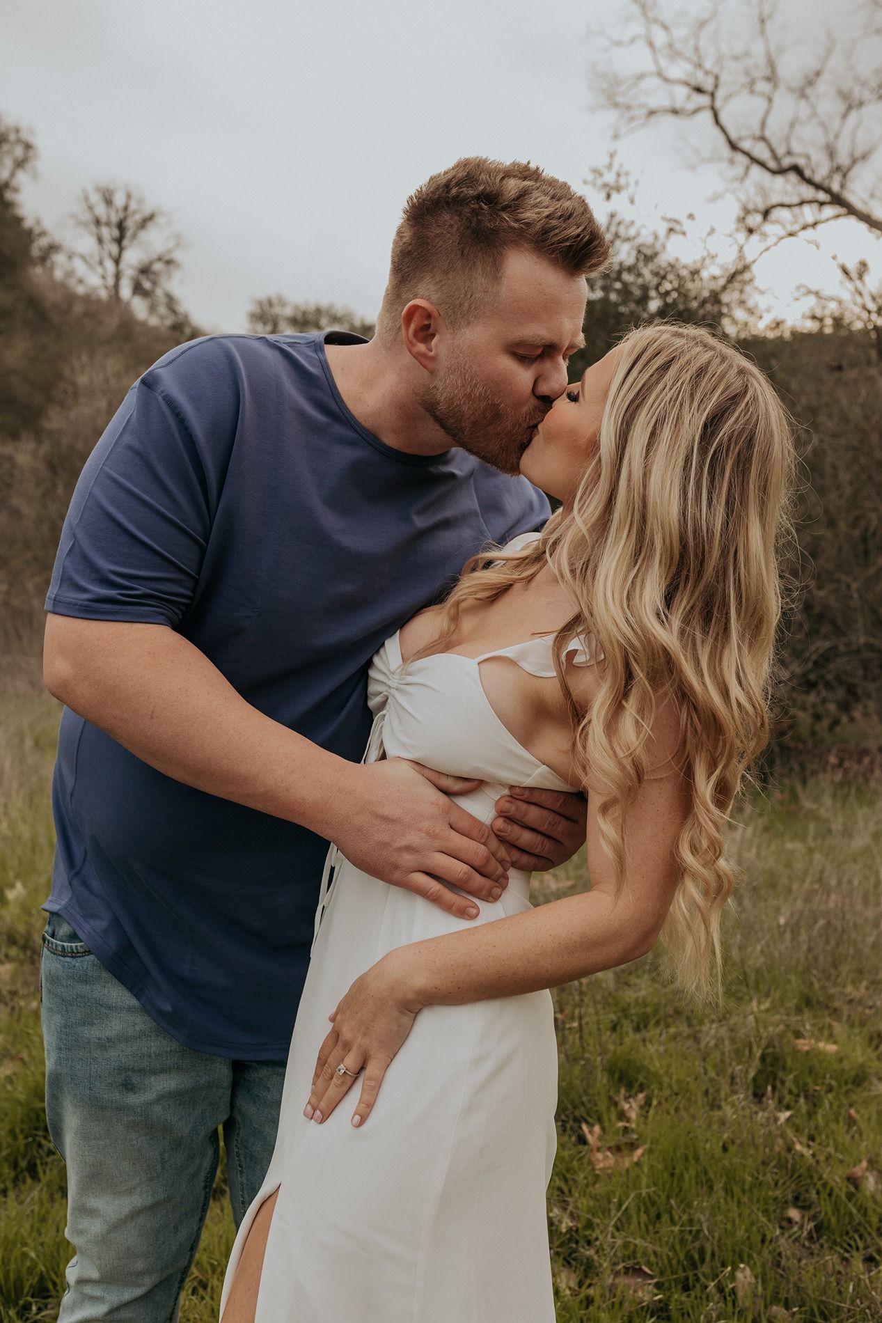A couple shares an intimate moment together in a natural outdoor setting with tall grass and trees in the background in San Diego.