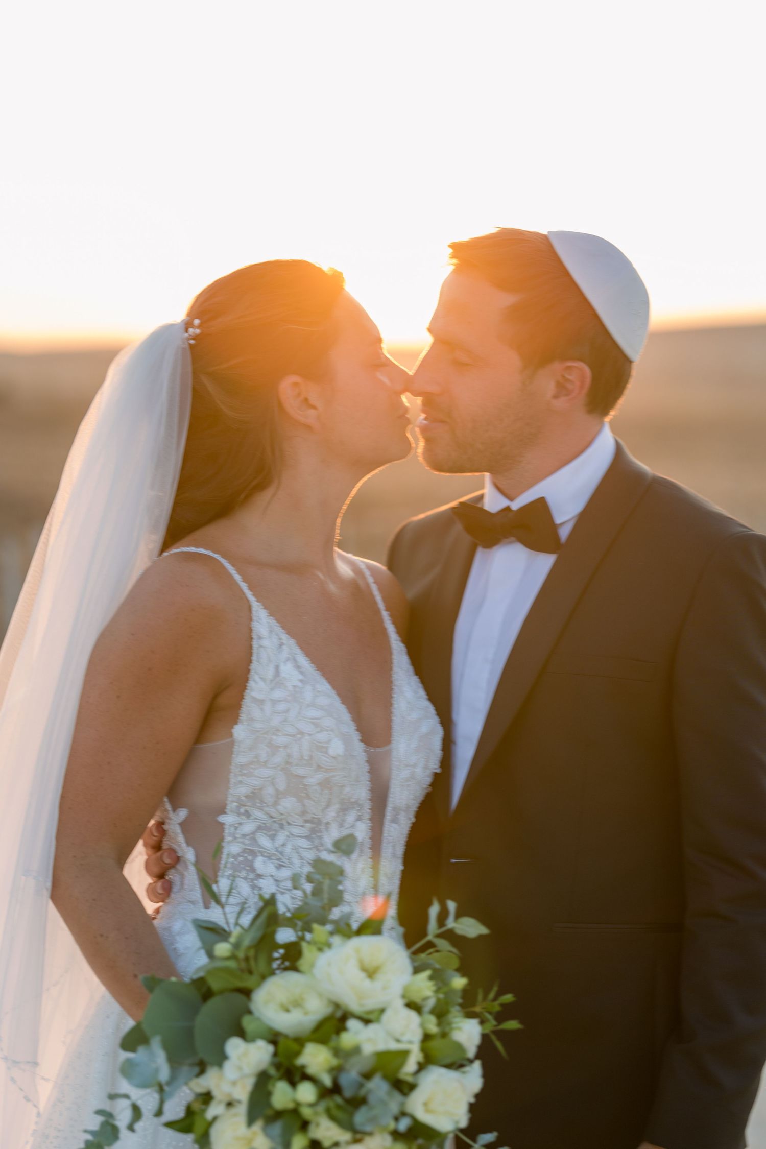 Newlyweds share an intimate moment at golden hour with white floral bouquet.