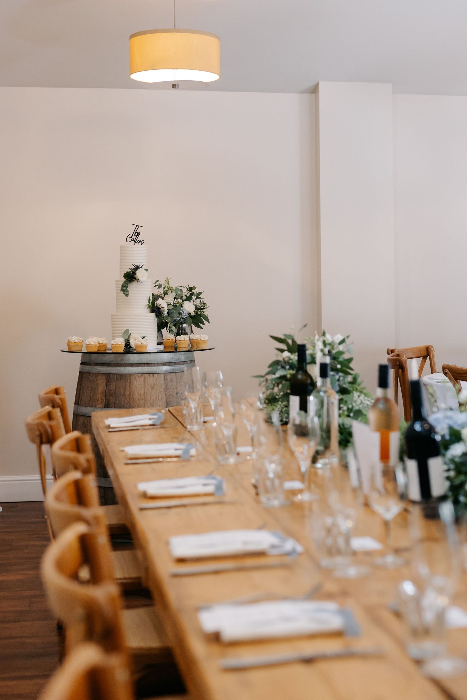 A long wooden dining table set with white plates and wine glasses features minimalist decor and tan chairs in a restaurant setting.