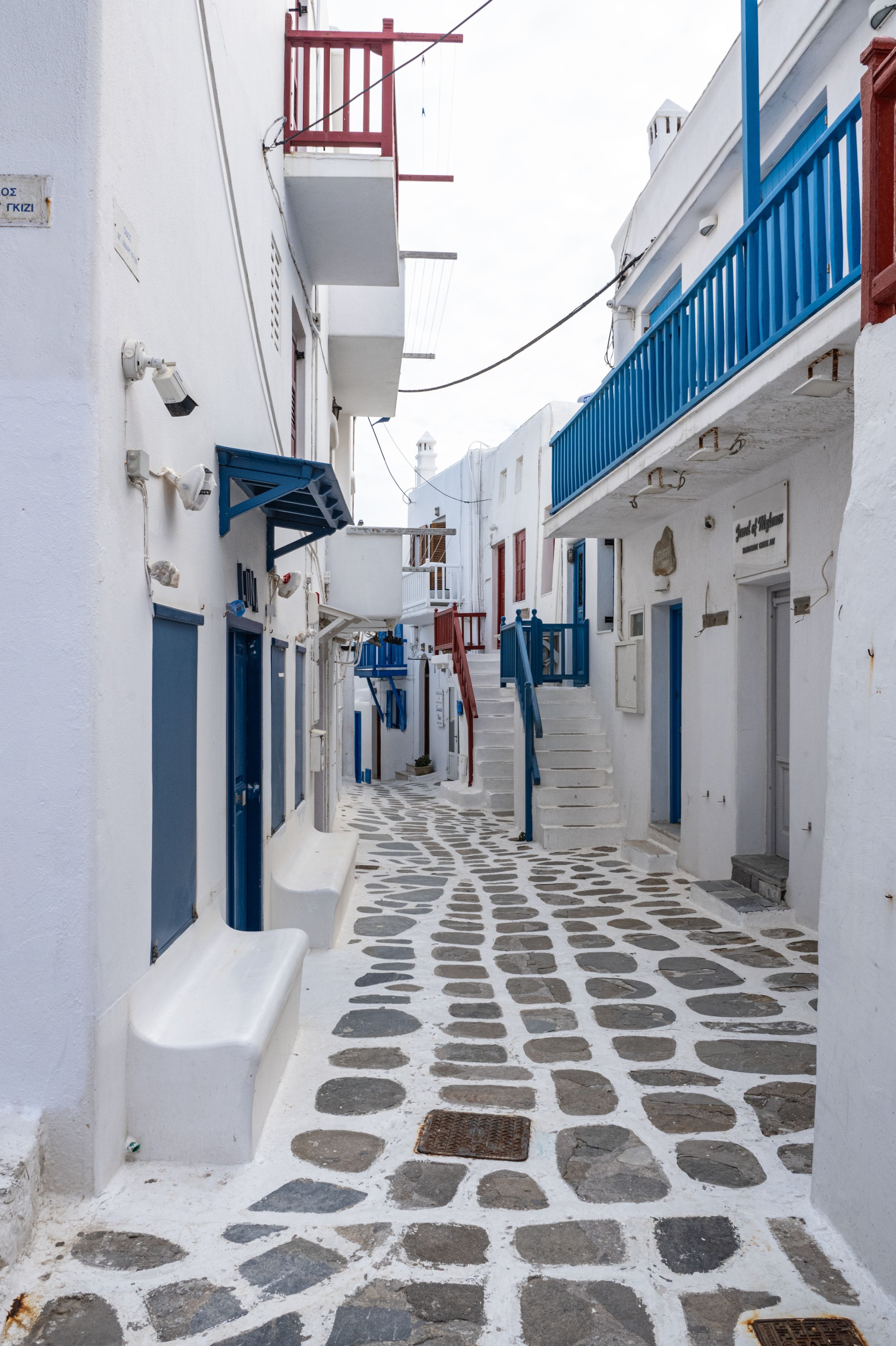 Narrow cobblestone alley with whitewashed walls and blue accents in traditional Greek architecture style.