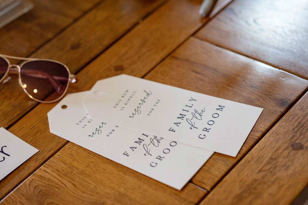 Wedding seating tags labeled Family of Groom displayed on a wooden table beside aviator sunglasses.