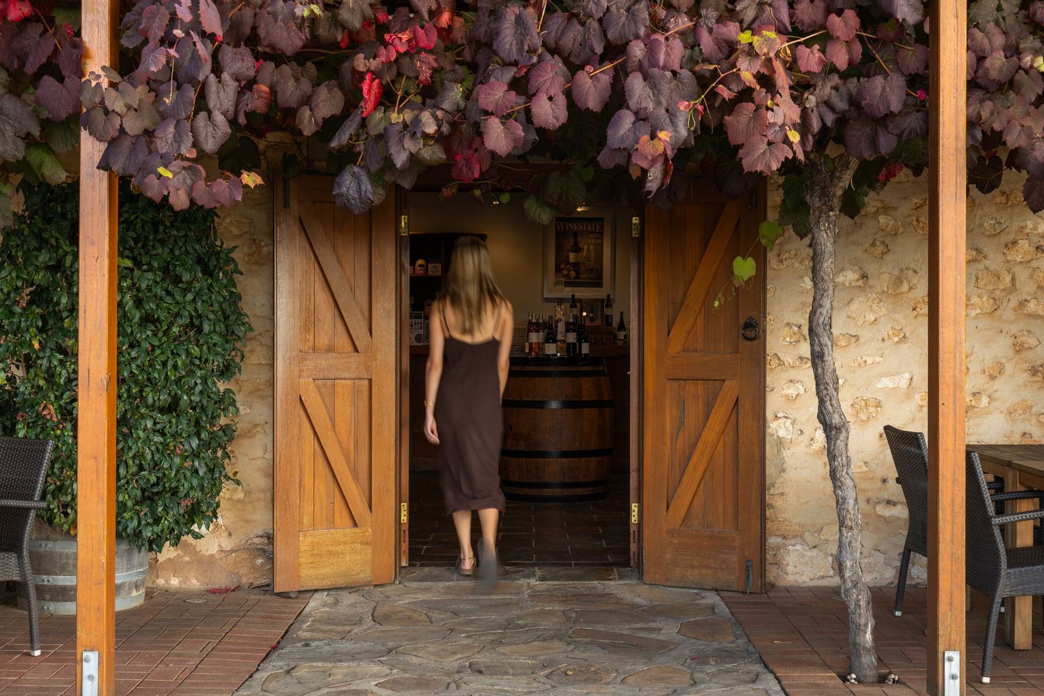 Woman walking into rustic winery cellar door with autumn vines overhead
