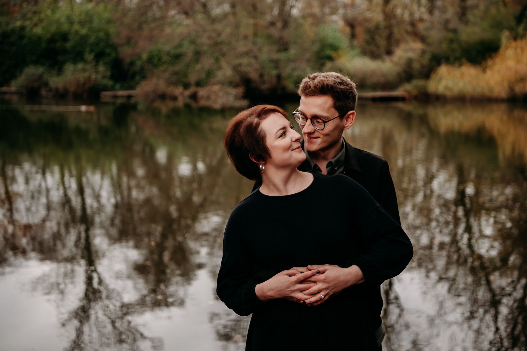 Romantic couple shares intimate moments by a tranquil lake during an autumn engagement photoshoot.