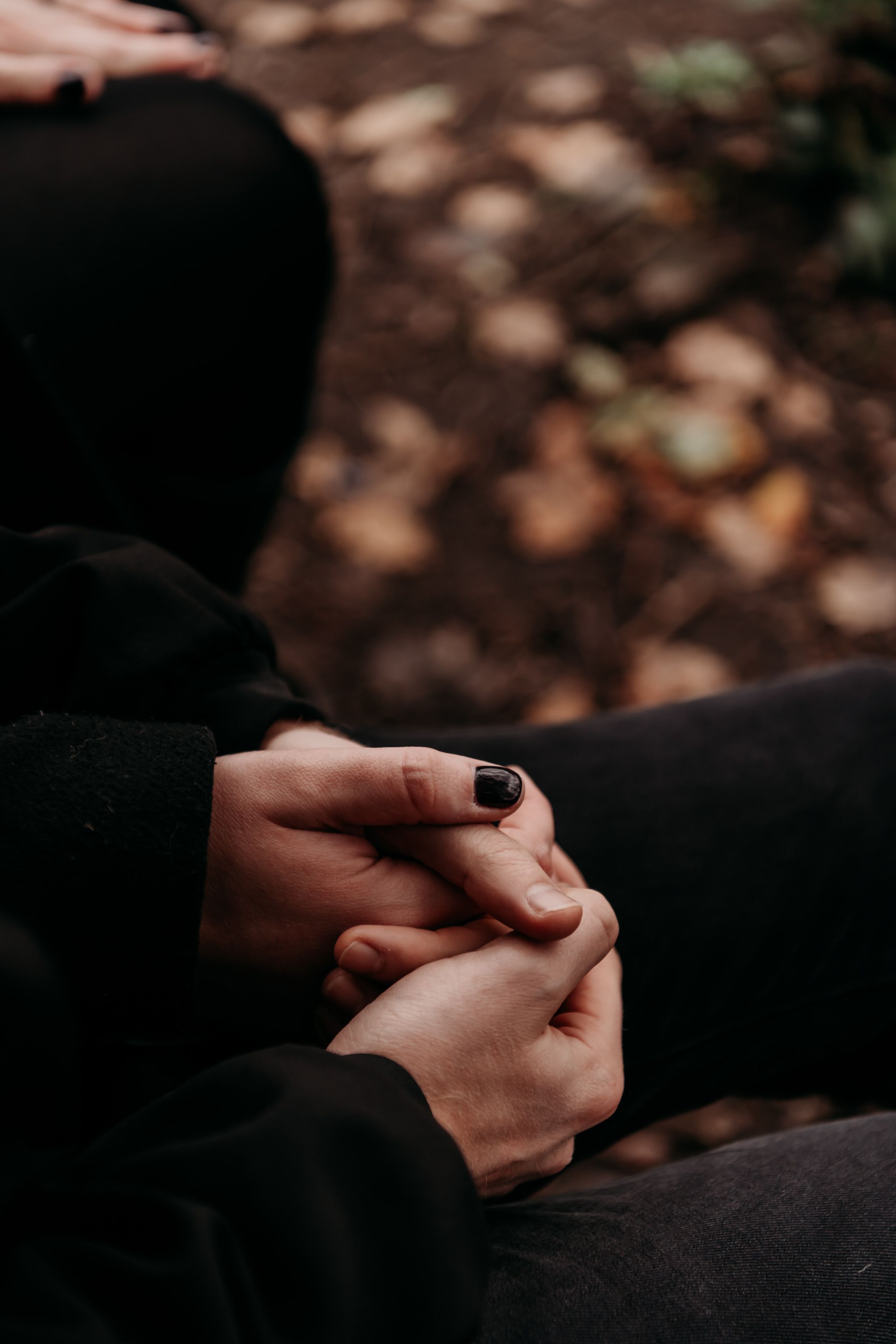 Close-up of hands holding each other tenderly against a dark background.
