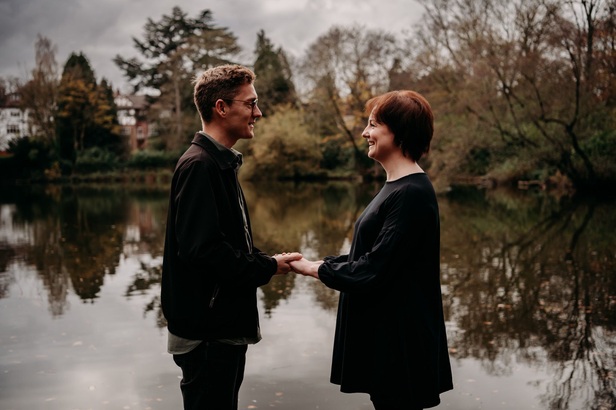Two people share an intimate moment by a tranquil lake surrounded by autumn trees and reflective waters.