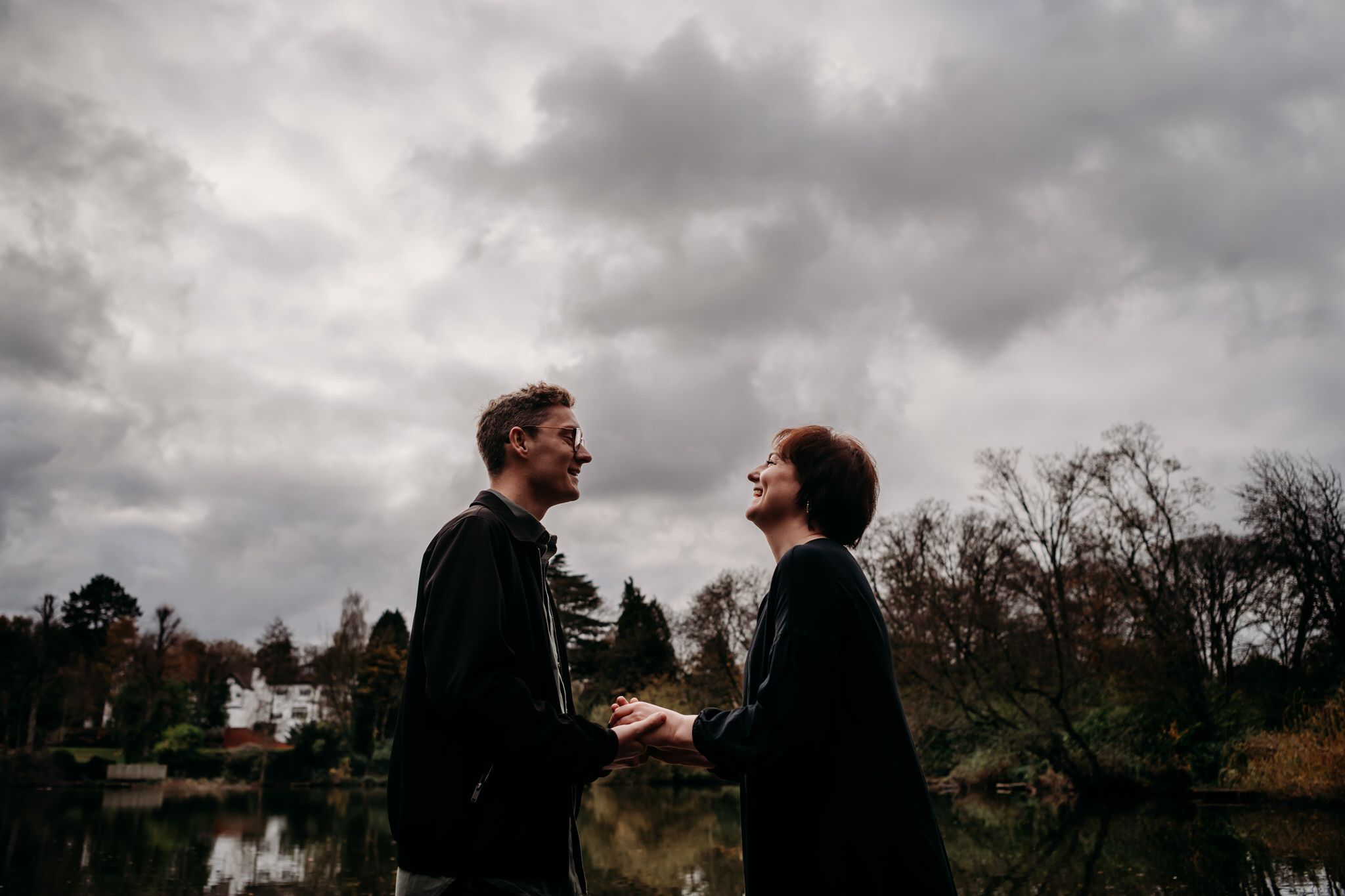 A silhouetted couple stands against a moody cloudy sky during golden hour.
