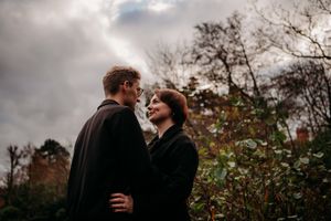 Romantic autumn photoshoot by a lake with overcast skies and fall colors in the background.