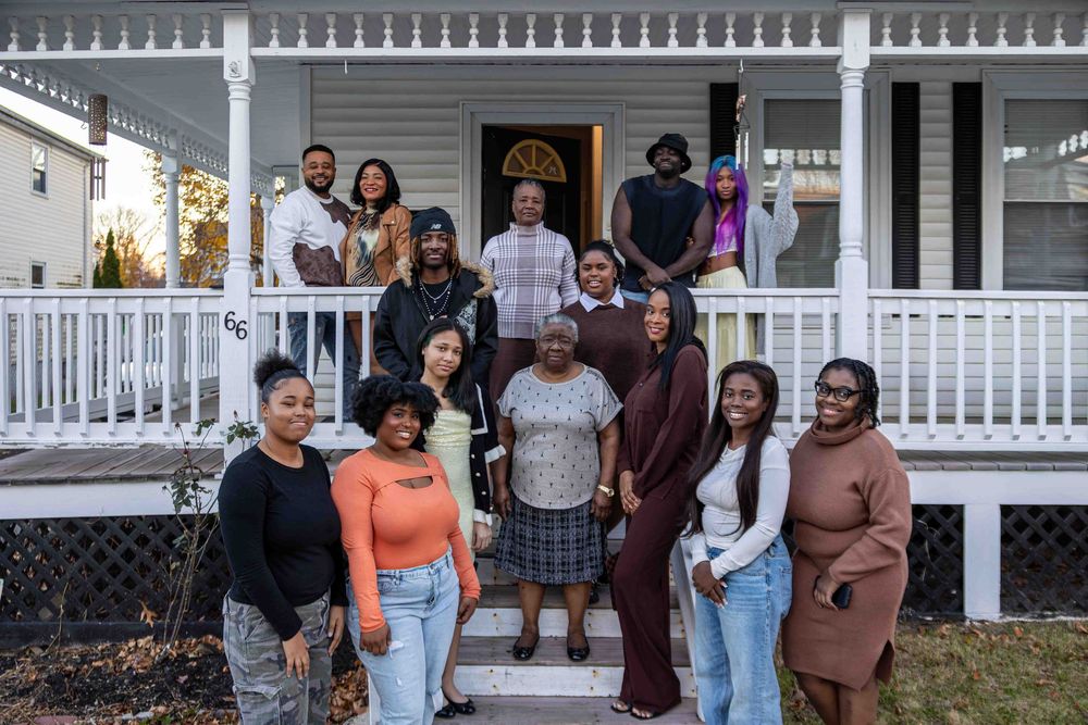 A group of people standing together on a porch with white railings during what appears to be a family gathering.